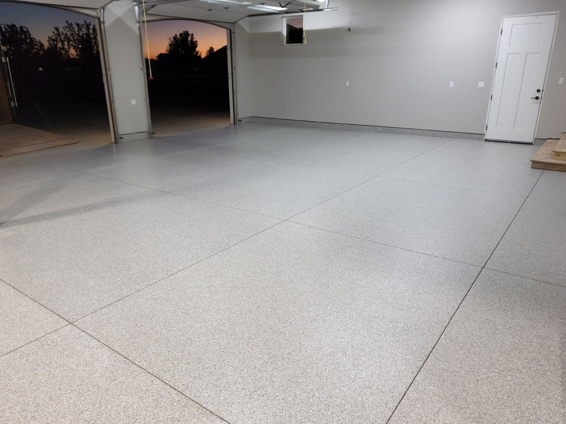 A new, gray, garage floor. Two garage bays are open on the left and the end of a sunset is visible.